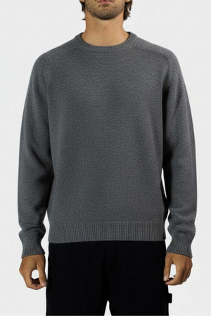 A person wears the Mr Simple Fred Knit, a relaxed fit, long-sleeve, crew neck gray 100% wool jumper with black pants against a plain light background, arms by their sides—ideal for any winter wardrobe. Face partially out of frame.