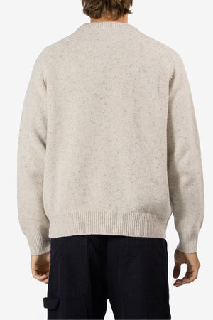 A person stands with their back to the camera, wearing the Mr Simple Fred Knit jumper—crafted from 100% wool—and black pants, showcasing a timeless winter look against a plain white background.