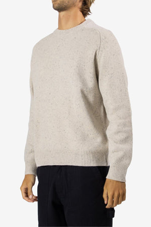 A person in a light beige Mr Simple Fred Knit 100% wool jumper with a crew neck and black pants stands against a white background. Their face is partially out of frame. Ideal for winter wardrobes.