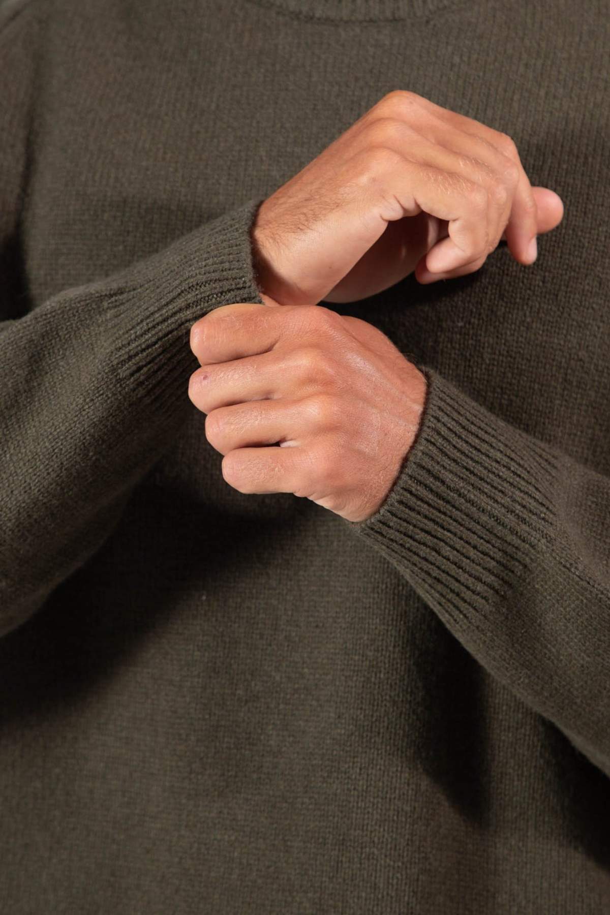 Close-up of a person wearing the Mr Simple Fred Knit in dark green, relaxed fit, adjusting one sleeve with the other hand. Only hands and upper torso are visible.