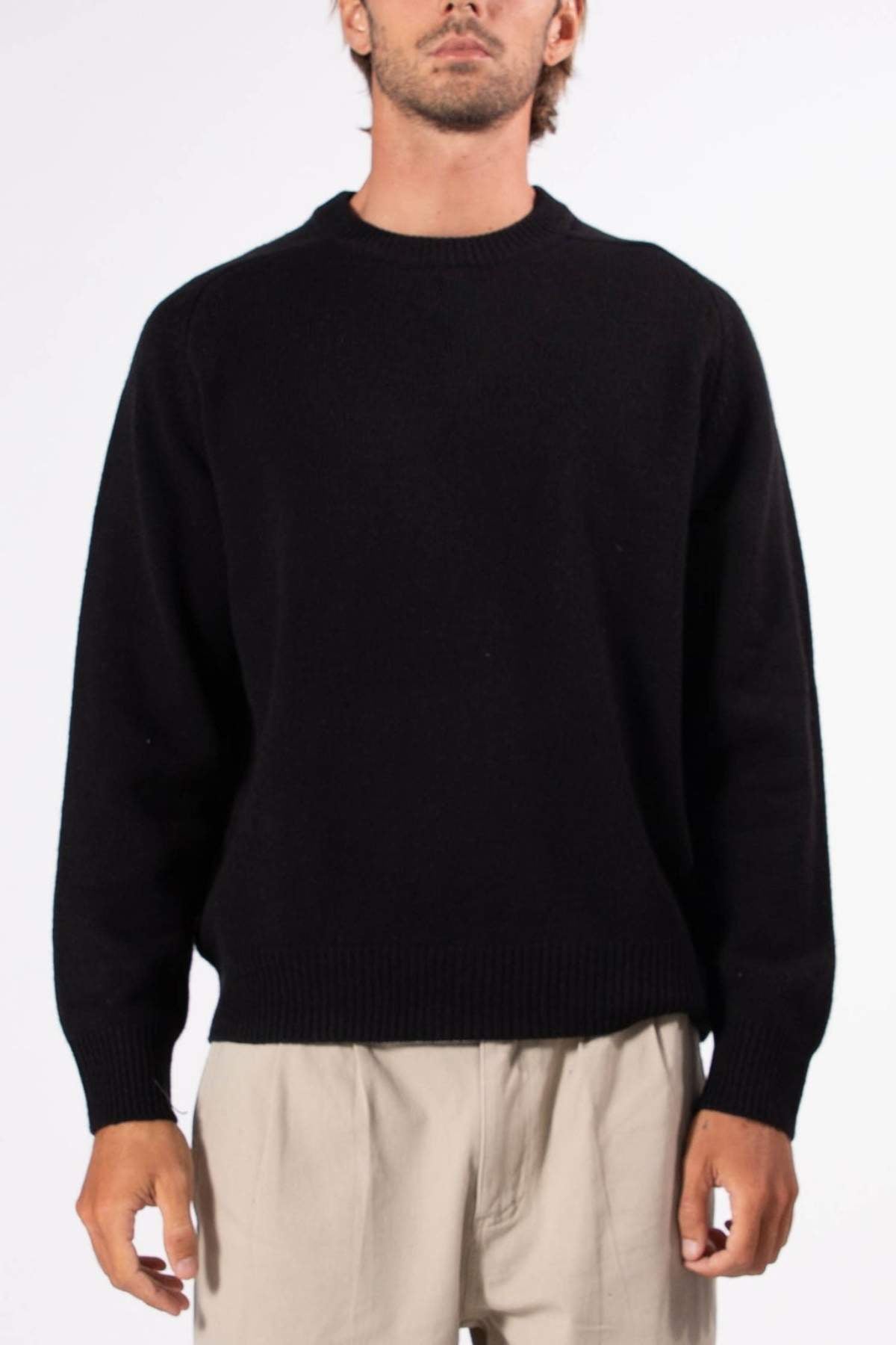 A person wears the Mr Simple Fred Knit, a relaxed fit black wool jumper, paired with light beige pants against a white background—a classic winter wardrobe staple.