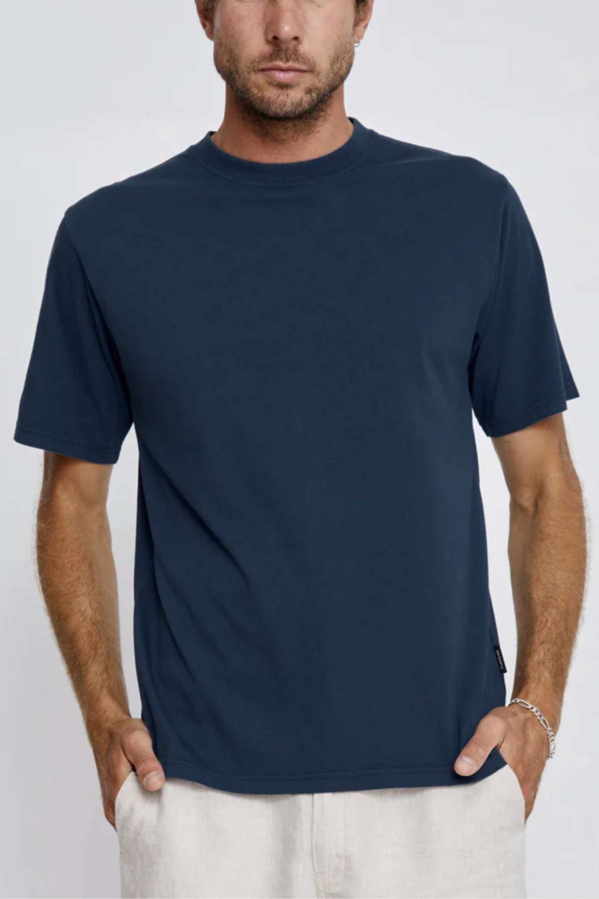 A man stands against a light background wearing the Mr Simple Heavy Weight Tee in dark blue with a boxy, loose fit and light-colored pants, hands in his pockets.