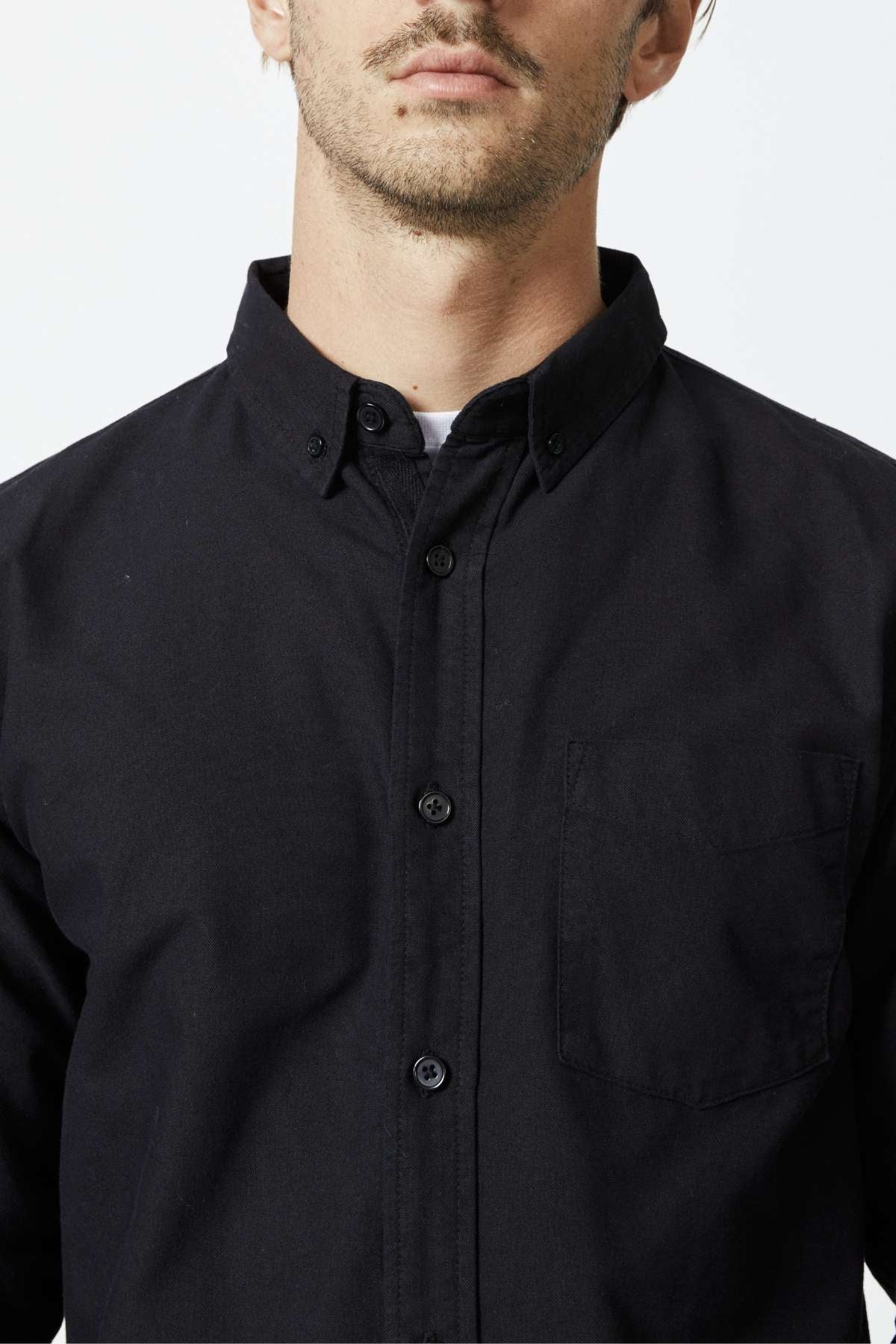 A man wears the slim fit Mr Simple Oxford Shirt in black organic cotton, featuring a chest pocket, shown from shoulders to just above the mouth against a plain light background.