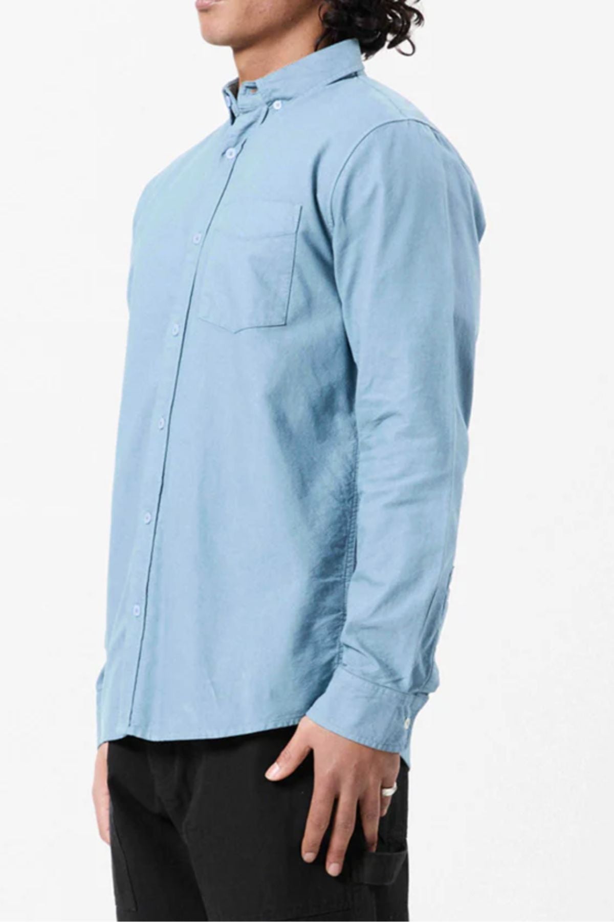 A person is wearing the Mr Simple Oxford Shirt in light blue, a slim-fit 100% cotton shirt with a front pocket, paired with black pants, standing sideways against a plain white background.