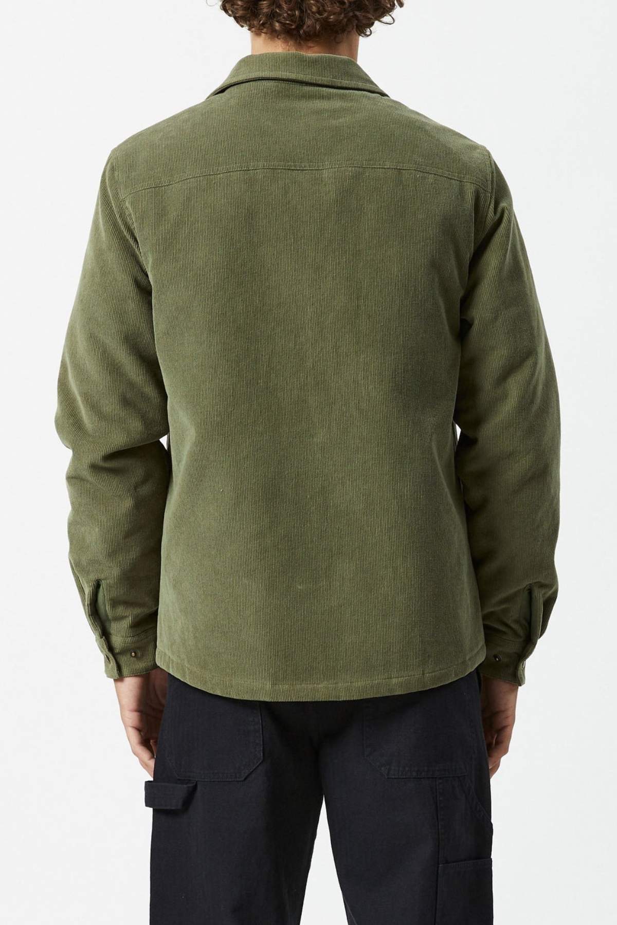 A person with curly hair is seen from the back wearing an olive green, long-sleeve Mr Simple Quilted Cord Jacket and black cargo pants against a plain light background.