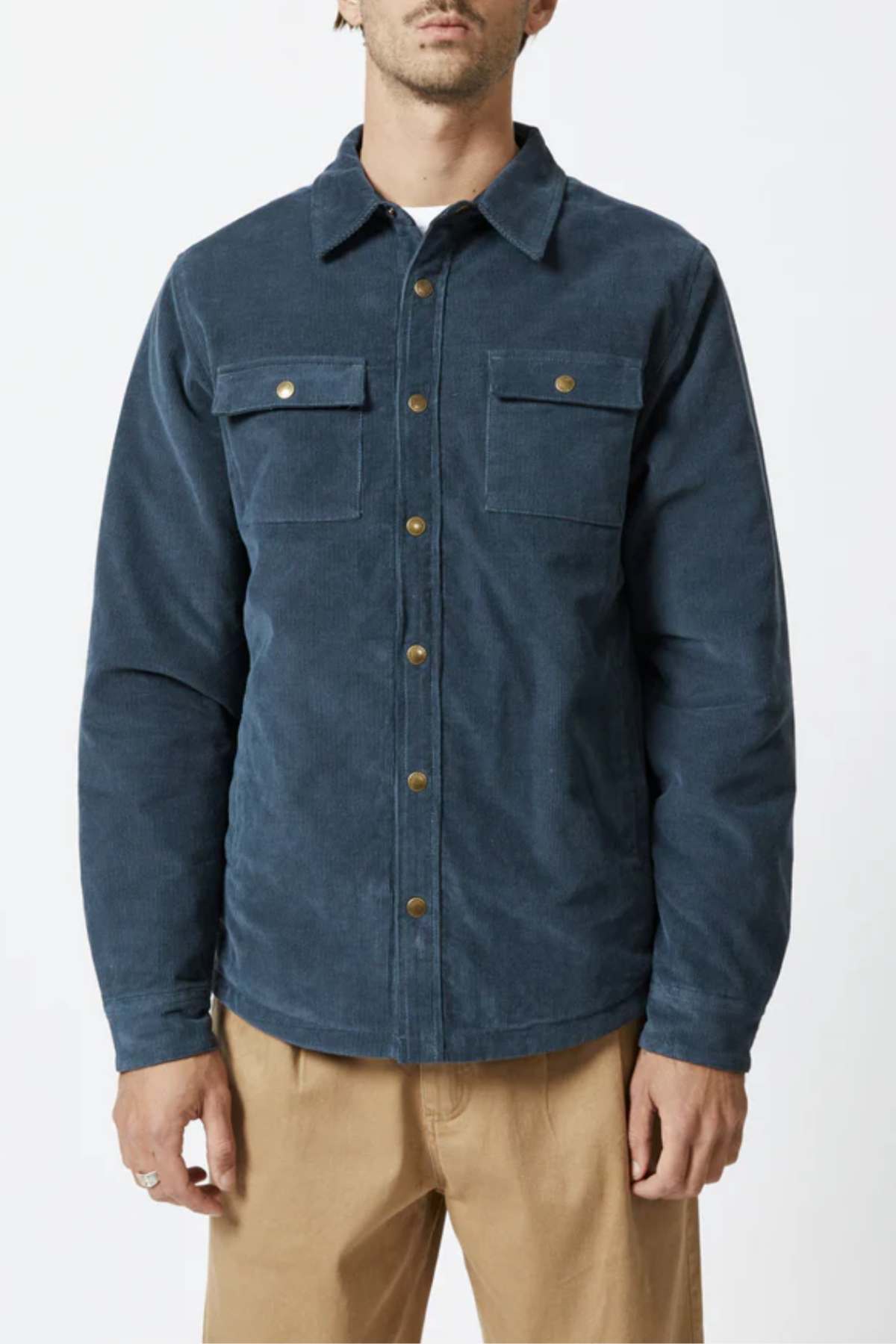 A person wearing a navy blue Mr Simple Quilted Cord Jacket with brass buttons and two chest pockets, paired with khaki pants, stands against a plain white background. The jacket, made from cotton corduroy with a relaxed fit, has a distinctive corduroy texture. The person's head is slightly out of frame.