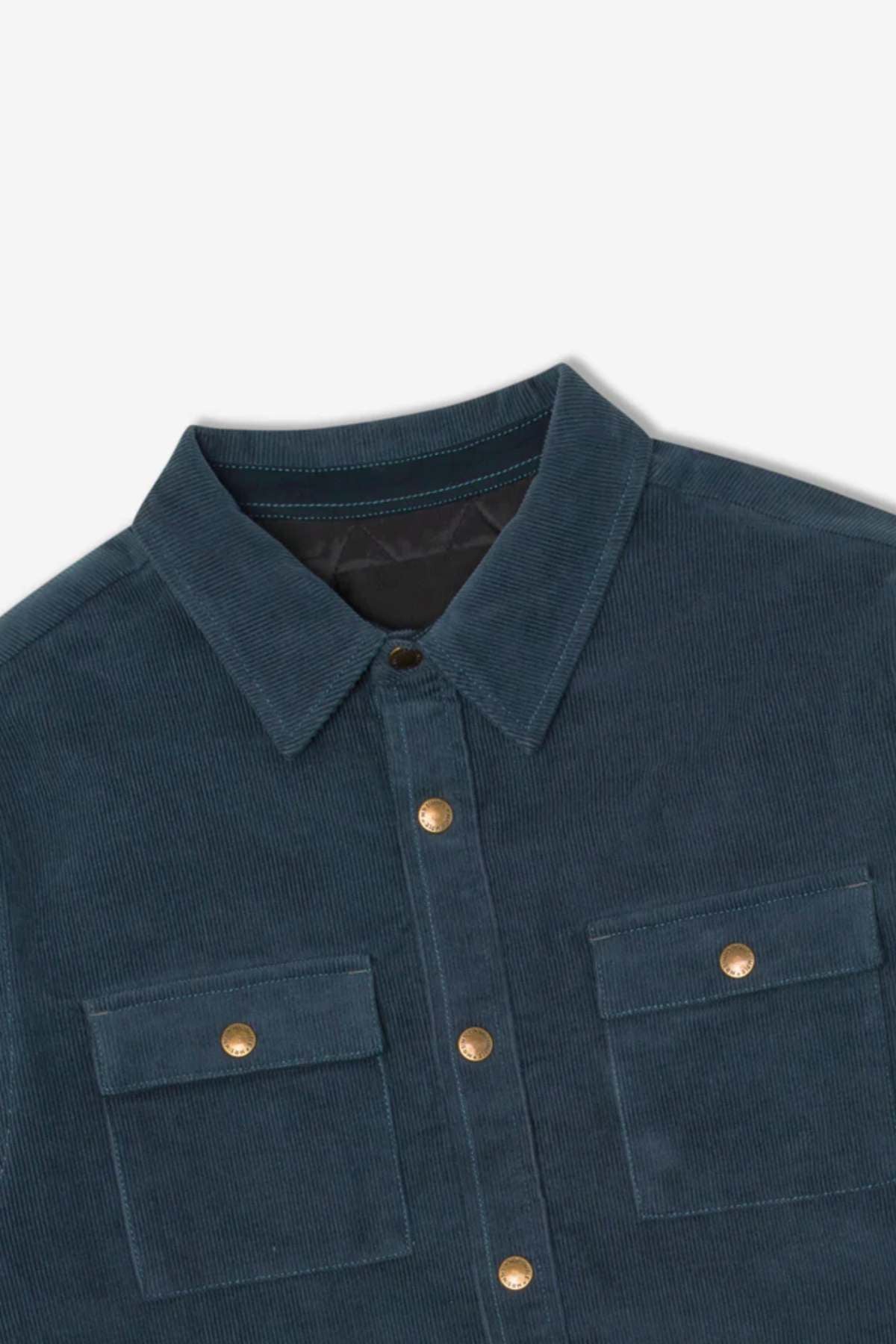 A close-up of the Mr Simple Quilted Cord Jacket in dark blue, showcasing its folded collar and two chest pockets adorned with gold buttons. The jacket, featuring a front closure with matching gold buttons, is laid flat on a white surface to emphasize its texture and details in its relaxed fit design.