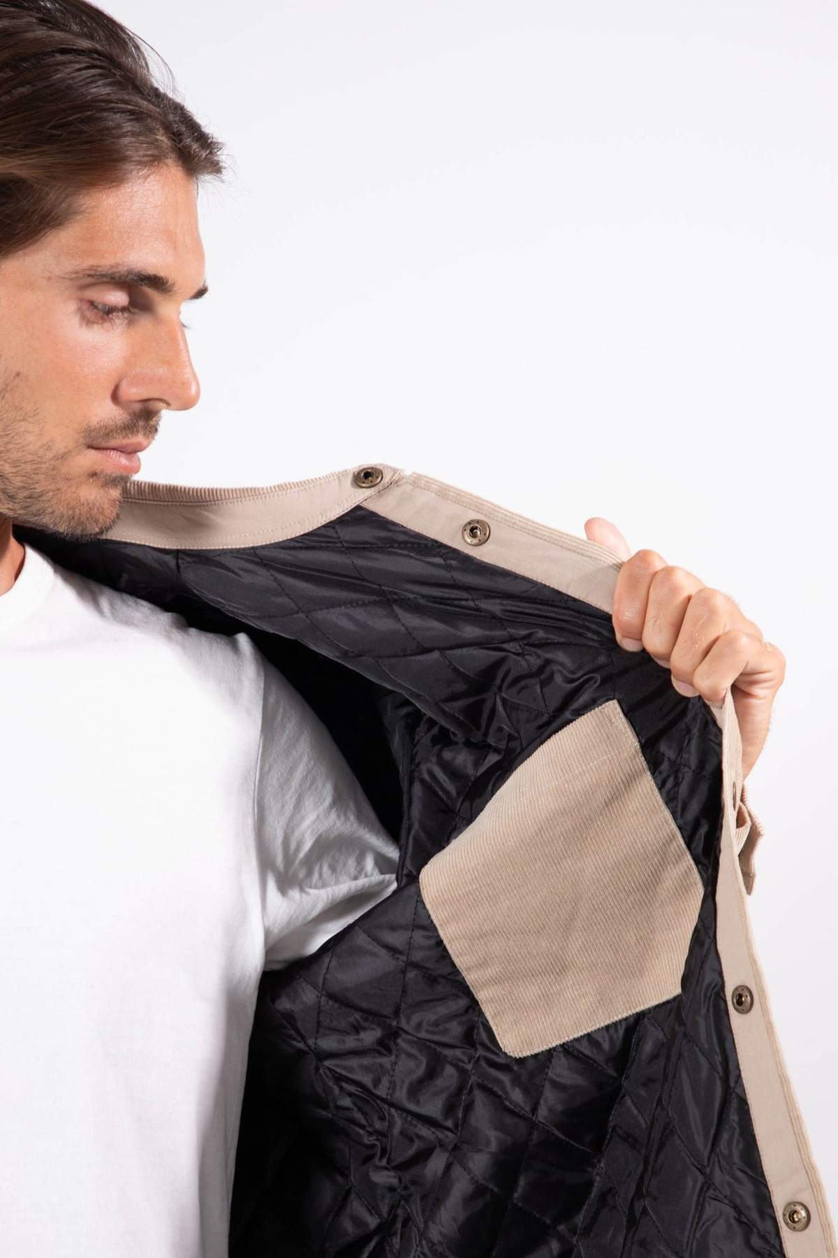 A man in a white shirt holds open the Mr Simple Quilted Cord Jacket, displaying its black quilted lining and light brown inner pocket, with the focus on the inside details of the beige jacket.