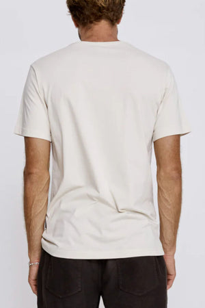 A man with short, light brown hair is seen from behind wearing the Mr Simple Reginald Organic Tee, a plain midweight t-shirt with a comfortable fit, along with dark pants against a neutral background.