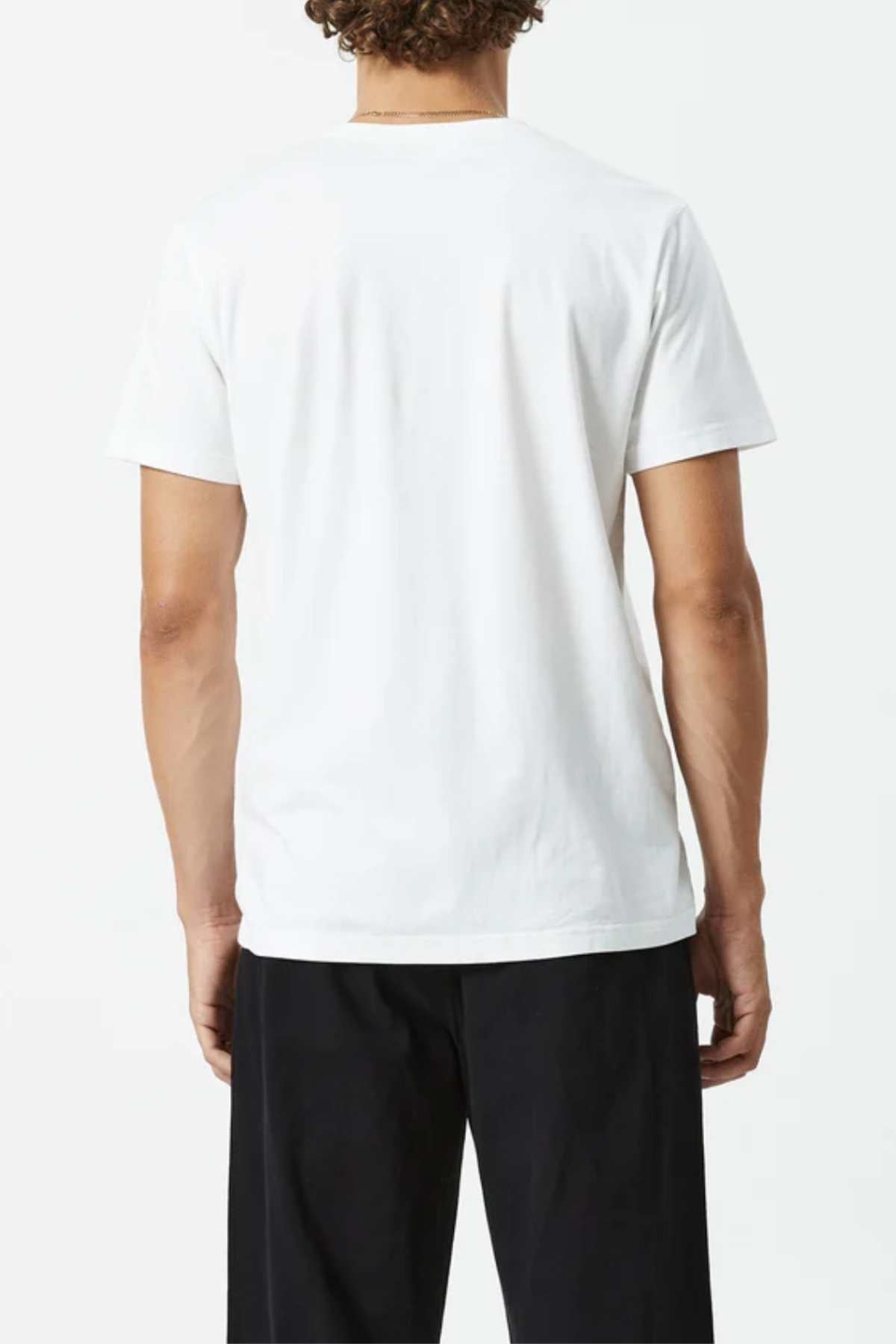 A person with short curly hair is shown from the back wearing the Mr Simple Reginald Organic Tee, a plain white 100% organic cotton midweight shirt, paired with black pants against a light background.