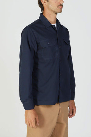 A man in a navy Mr Simple Ripstop Canvas Overshirt with chest pockets and tan pants stands against a plain light background, turned slightly to the side.