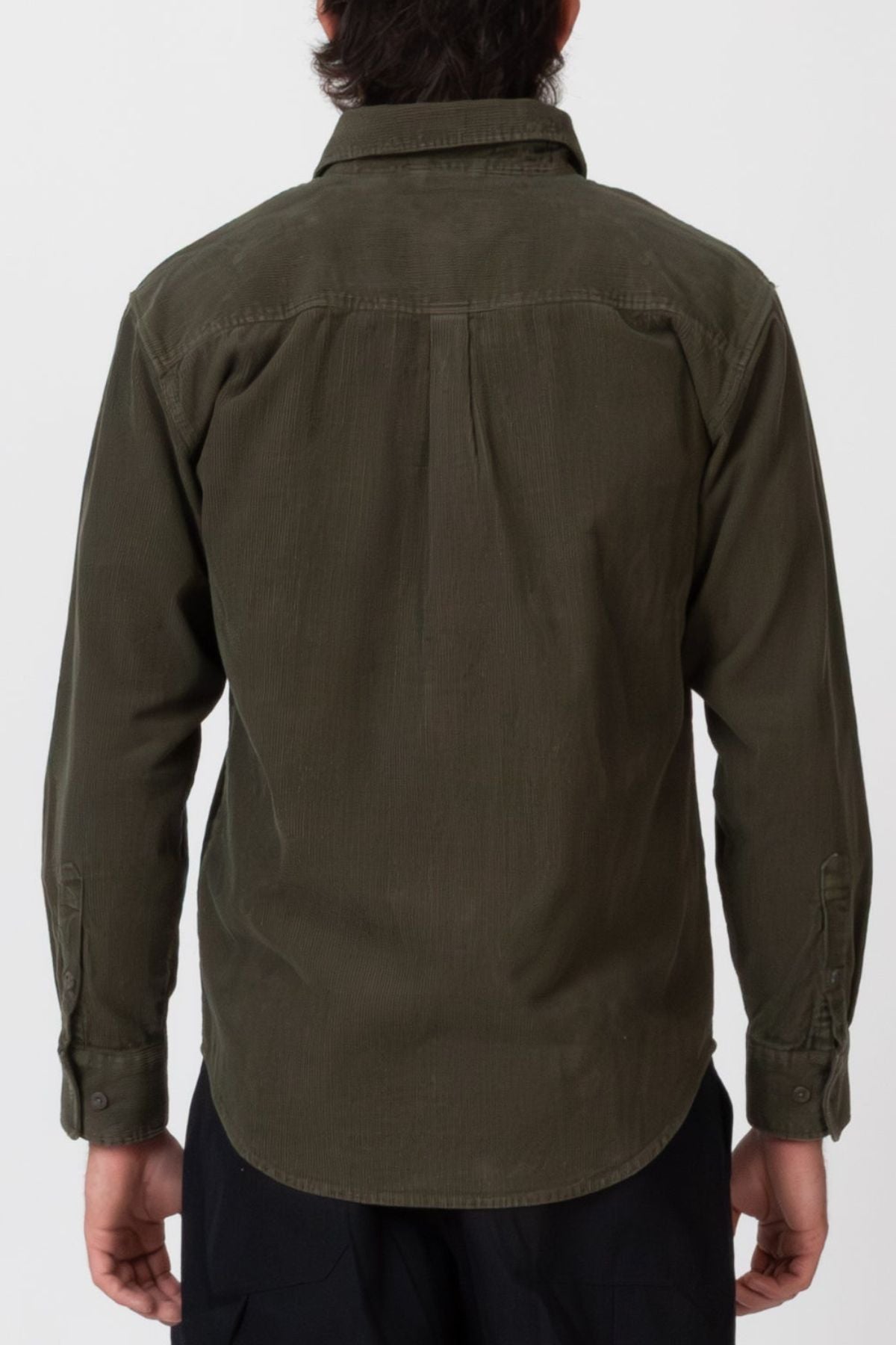 A person stands facing away from the camera, wearing the Mr Simple Sawyer Cord Shirt in olive green and black pants against a plain light background.