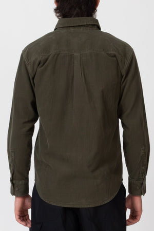 A person stands facing away from the camera, wearing the Mr Simple Sawyer Cord Shirt in olive green and black pants against a plain light background.