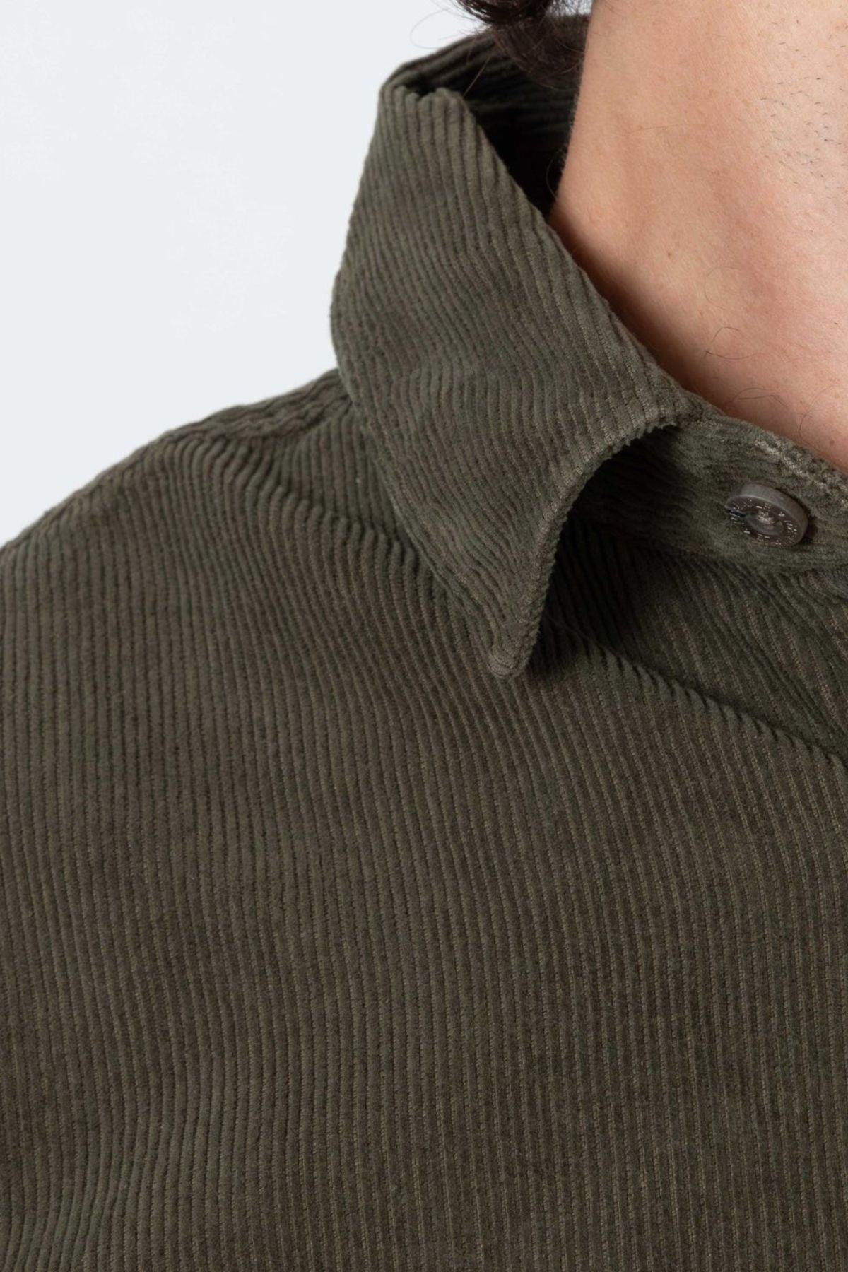 A close-up of a person wearing the Mr Simple Sawyer Cord Shirt in olive green organic cotton, showing the collar, button, and textured corduroy fabric. Only part of the neck, shoulder, and collar are visible.