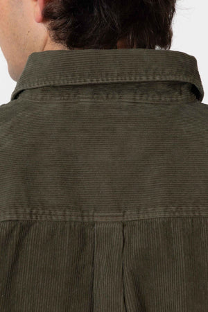 Close-up of the back of a person wearing the Mr Simple Sawyer Cord Shirt in olive green organic cotton, focusing on the collar and upper back, with only part of their head and hair visible.