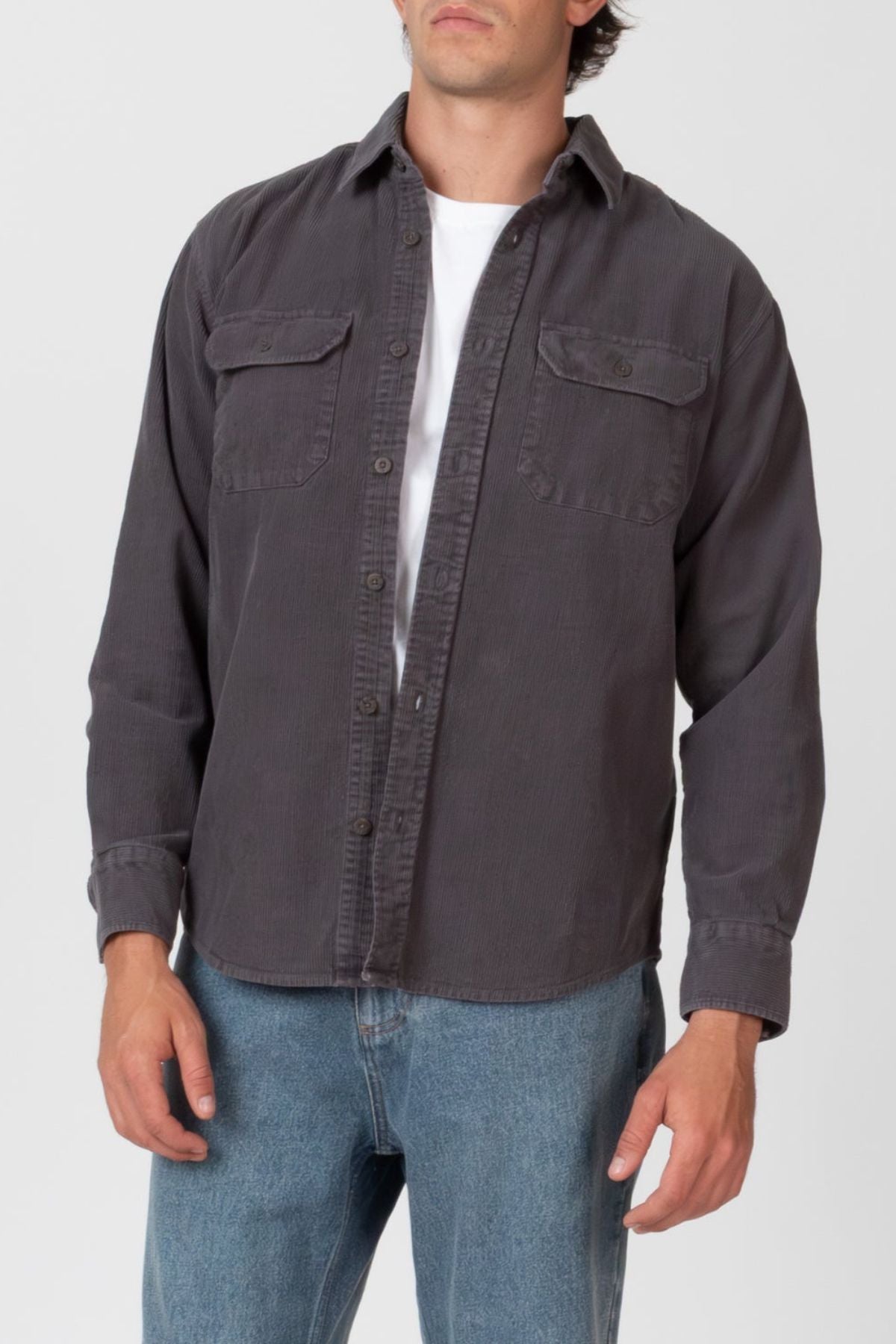 A man stands with his arms relaxed by his sides against a plain light background, wearing the Mr Simple Sawyer Cord Shirt in dark gray over a white tee with light blue jeans.
