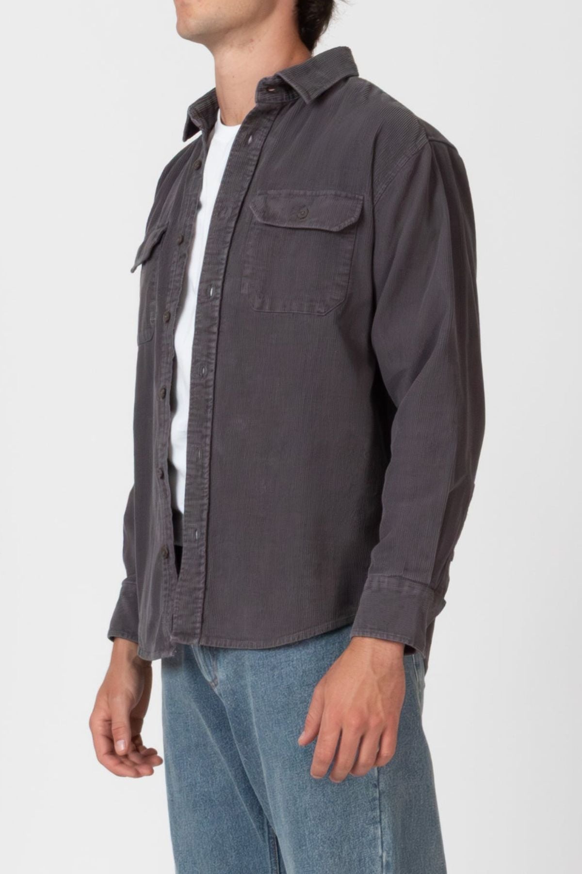 A person wearing the Mr Simple Sawyer Cord Shirt in dark gray over a white tee and blue jeans stands against a white background. The shirt features chest pockets, and the person's face is partially out of frame.