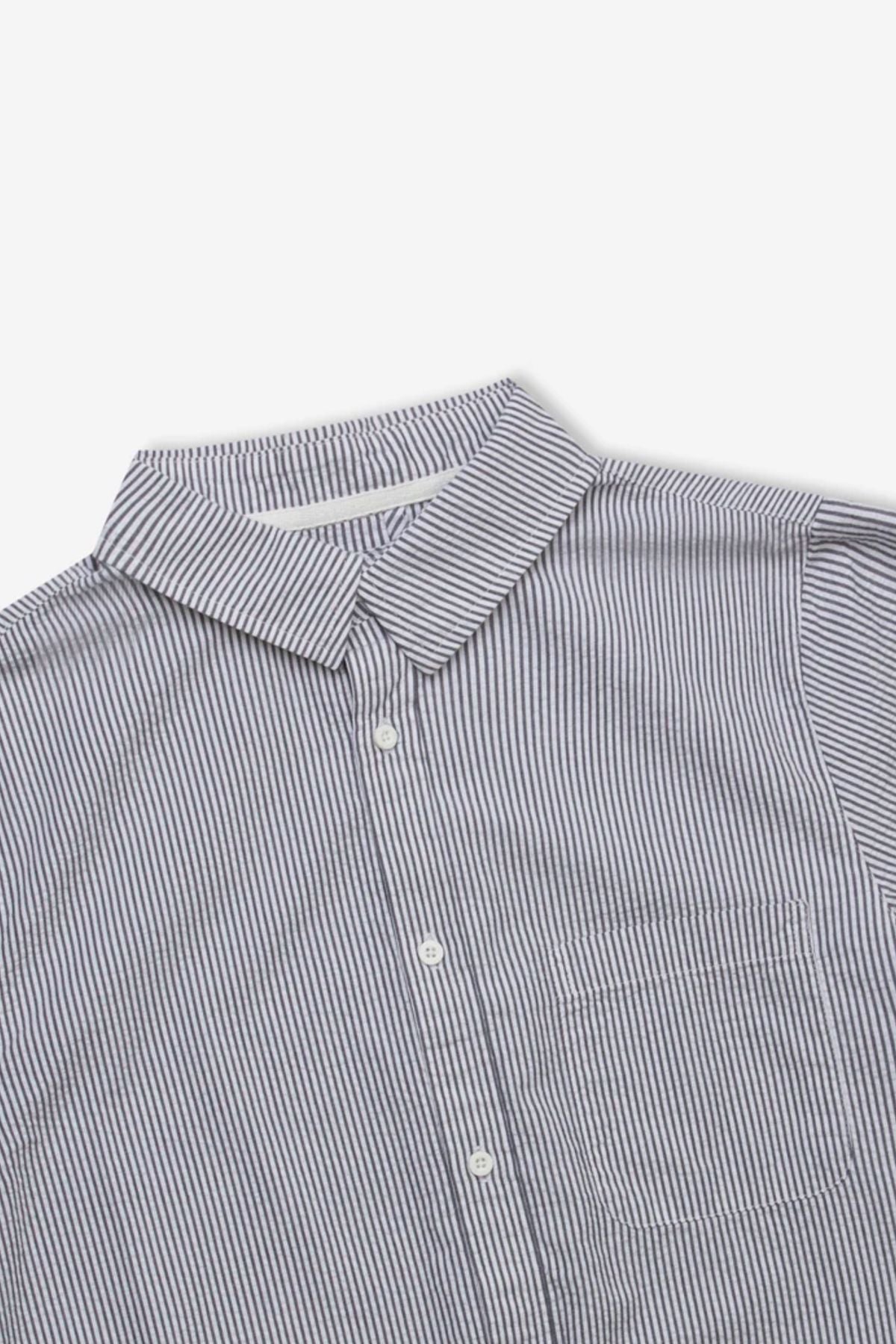 A close-up of the Mr Simple Seersucker Short Sleeve Shirt, featuring thin blue and white vertical stripes, collar, white buttons, and chest pocket—laid flat on a white background for a fresh summer look.