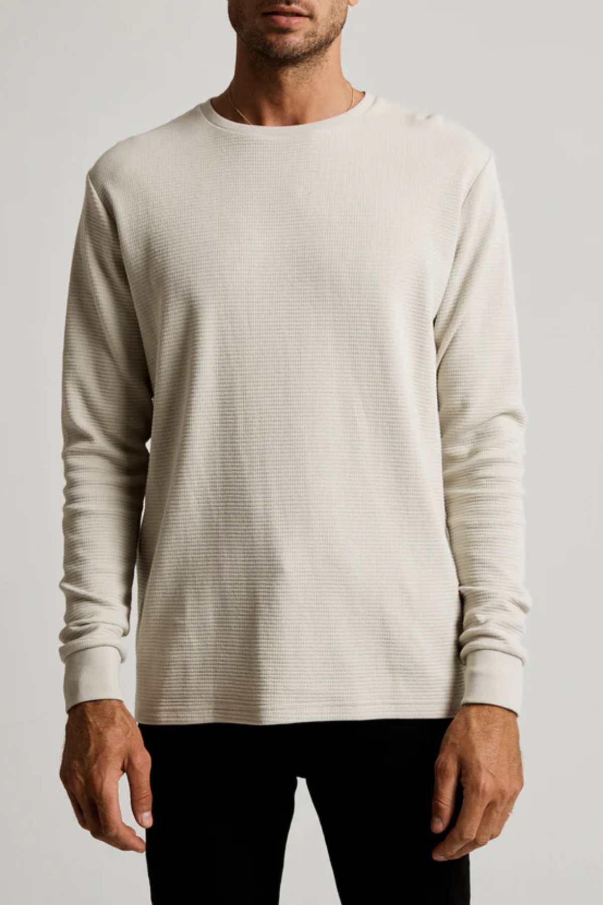 A man wearing a Mr Simple Smith Waffle cream long-sleeved shirt, crafted from organic cotton for a classic fit with a crew neckline, stands against a plain background. He is also in black pants.