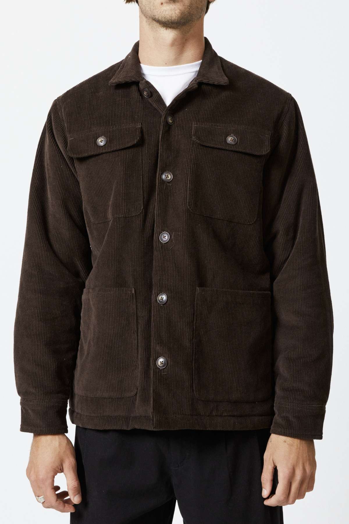 A person wears a Mr Simple Stockyard Sherpa Jacket with a full button front and dark brown corduroy texture. Made of 100% cotton outer, it features two chest pockets and two lower pockets. It's layered over a crisp white shirt, though their face remains out of view.