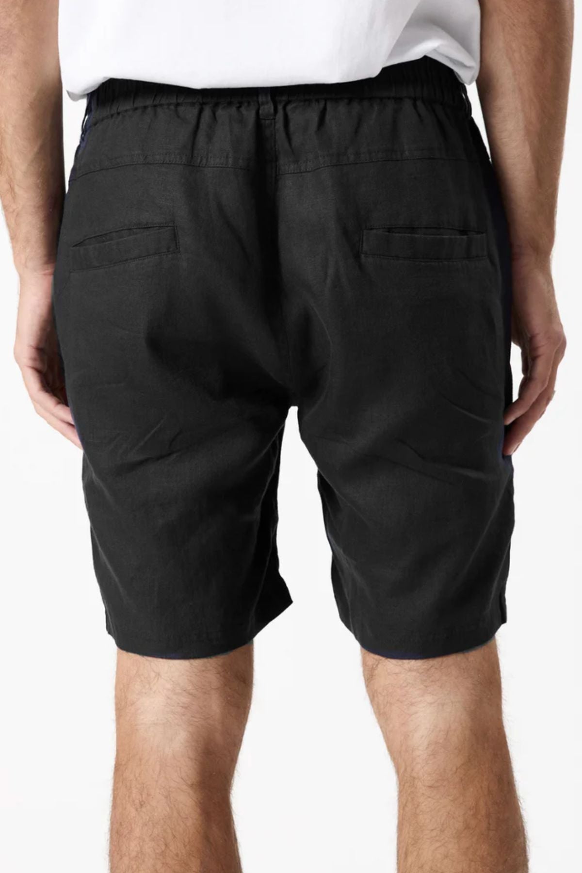 A person is shown from the back wearing Mr Simple Tanner 3.0 Linen Shorts in black, featuring an elastic waistband, two back pockets, and a comfortable fit, paired with a white shirt.