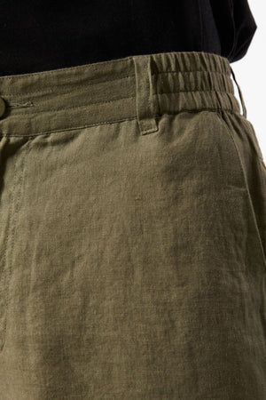 Close-up of the waistband and upper section of the Mr Simple Tanner 3.0 Linen Short in olive green, featuring a breathable elastic waistband and button, paired with a black top.