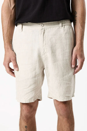 A person wears the Mr Simple Tanner 3.0 Linen Short in light beige with an elastic waistband and a black shirt, standing with arms relaxed at their sides; photo is cropped from waist to just above the knees.