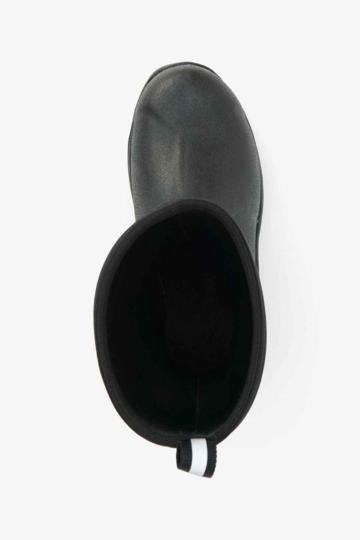 Top view of a single Muck Boot Muckmaster Mid Boot in black featuring a black and white pull tab at the back. The boot is empty and showcases a textured, solid MS-1 molded outsole for enhanced grip. Made of waterproof material, the interior is visibly dark, providing contrast with the durable outer material.