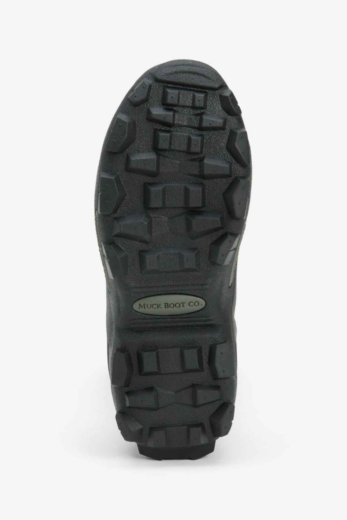 Close-up of the sole of a Muck Boot Muckmaster Mid Boot, showcasing an aggressive tread pattern and deep lugs for traction. A small label near the center reads "Muck Boot Co." The boot, featuring an MS-1 molded outsole and neoprene construction, appears designed for rugged outdoor use. The background is white.