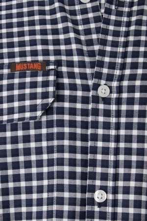 Close-up image of the Mustang Signature Check Shirt for men, crafted from high-quality cotton and featuring a black and white checkered pattern with a pocket on the left side. The word "MUSTANG" is embroidered in red on the pocket, showcasing Mustang's signature style. The shirt also has white buttons down the front.