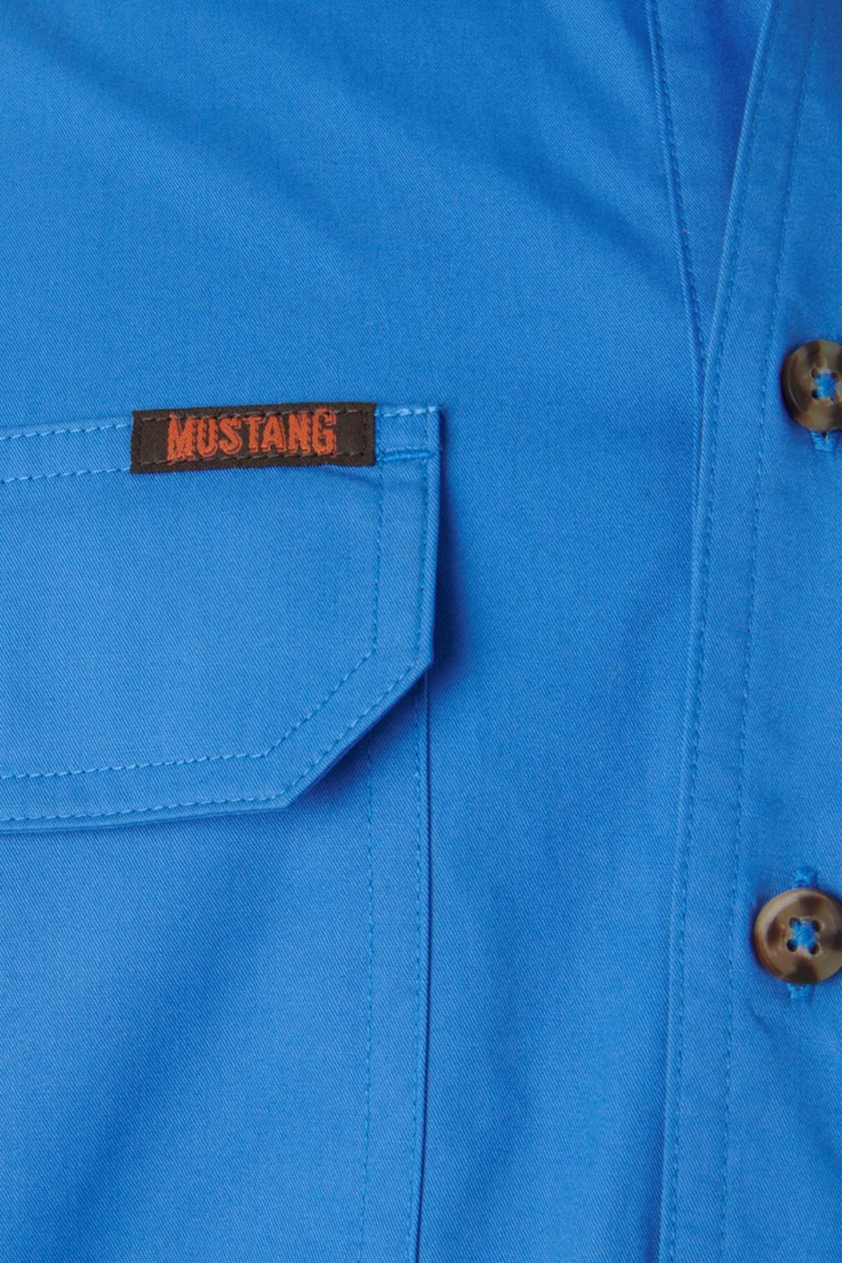Close-up of a blue cotton fabric with a left pocket featuring a "Mustang" tag in red. Brown marbled buttons to the right enhance the charm of this durable Men's Mustang Signature Closed Front Workshirt.