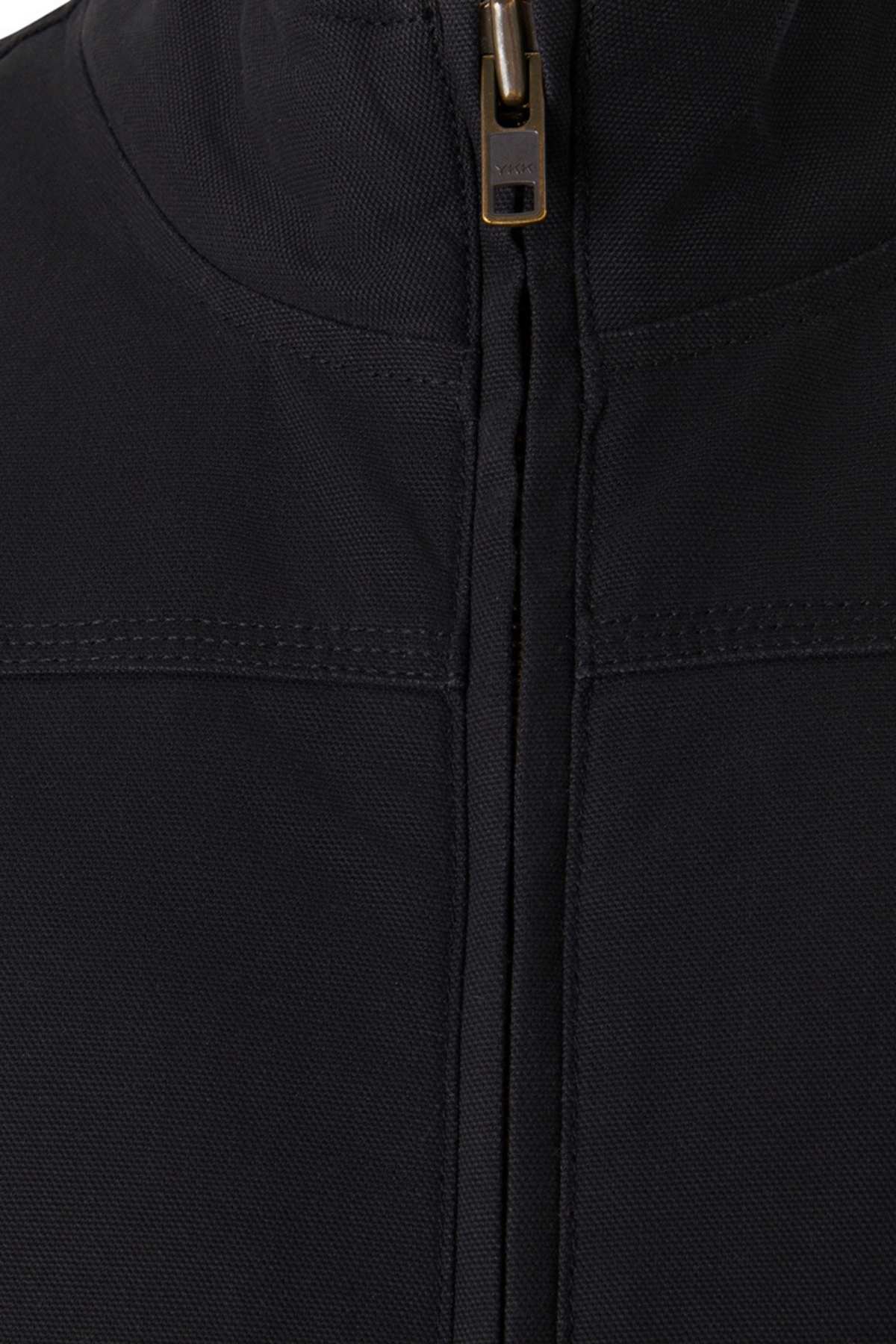 Close-up view of the Mustang Signature Outback Canvas Vest in black, featuring a brass-colored zipper partially visible at the top. The durable canvas material showcases a high collar and seam detail across the chest area, highlighting its sturdy and textured fabric.