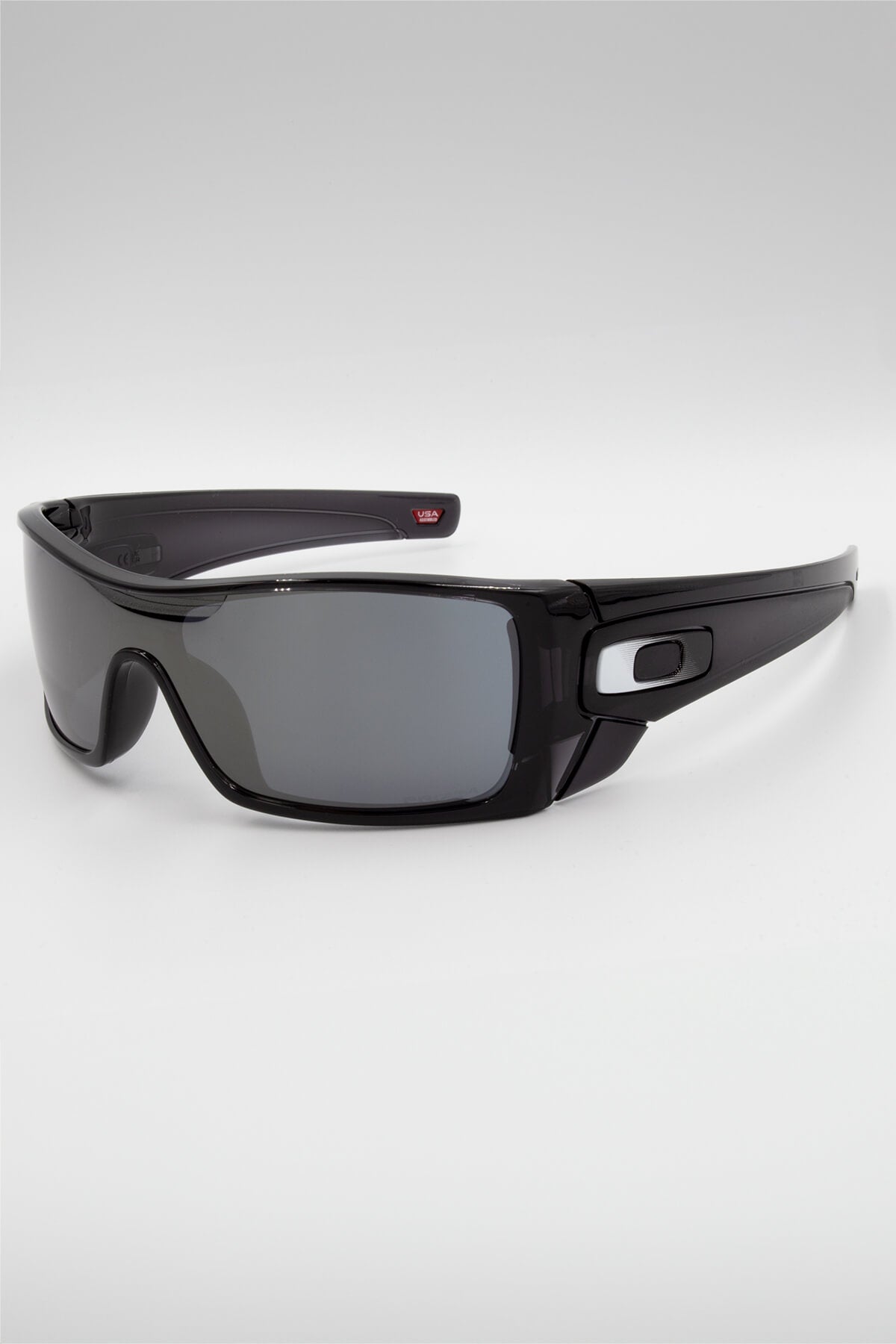 Oakley Batwolf sunglasses feature a black wraparound design, shiny finish, and thick arms with a stylized "O" logo. The dark lenses with HDO™ technology offer a slight reflection. Set against a neutral gray background, these shades are sleek and modern.