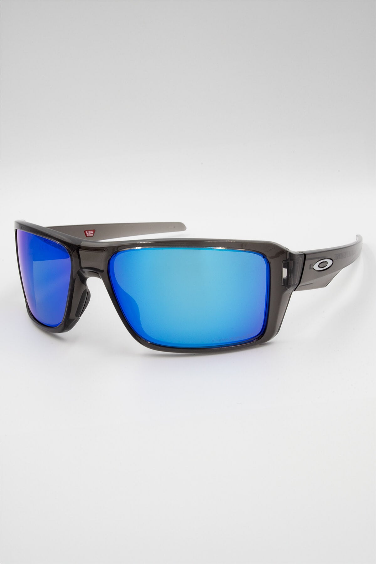 The Oakley Double Edge sunglasses, with dark rectangular frames and reflective blue polarized lenses, are strikingly displayed against a plain white background, capturing the sleek style of Grey Smoke.