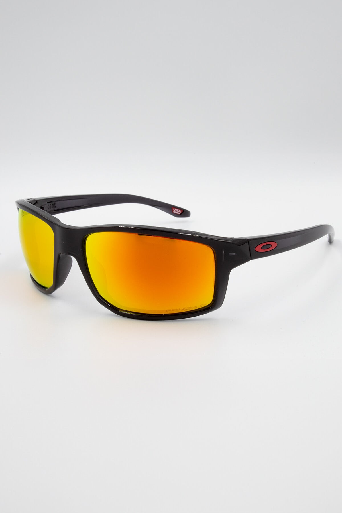 A pair of Oakley Gibston Polarized sunglasses, featuring black frames with orange-red mirrored Prizm lenses and red “O” logos on the temples, shown against a white background.