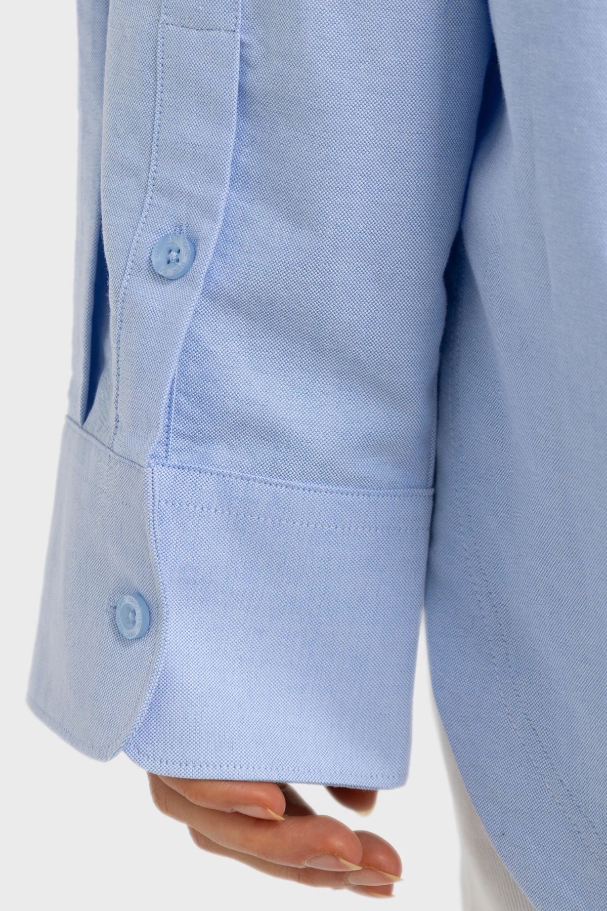 A close-up of a person’s hand and the cuff of a light blue ORTC Adelaide Oxford Shirt, with two blue buttons visible on the sleeve.