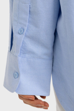 A close-up of a person’s hand and the cuff of a light blue ORTC Adelaide Oxford Shirt, with two blue buttons visible on the sleeve.