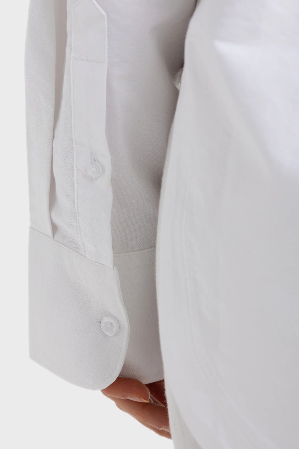 A close-up of a person’s arm wearing the ORTC Adelaide Oxford Shirt in white showcases the sleeve cuff with two white buttons. The visible portion of the hand beneath the cuff highlights the shirt’s premium cotton fabric and meticulous attention to detail.