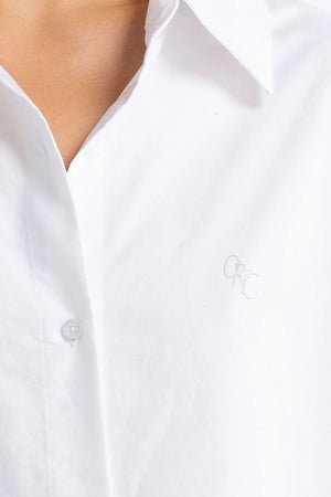 A close-up of a person wearing the ORTC Adelaide Oxford Shirt, featuring premium white cotton with a crisp collar and a small embroidered logo on the left chest. The shirt is buttoned up, showcasing its smooth and clean fabric.
