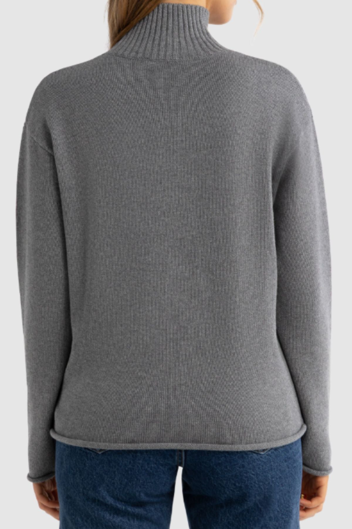 A person is seen from behind wearing a gray ORTC Astrid Knit Sweater with a high neck and blue jeans, set against a plain light background.