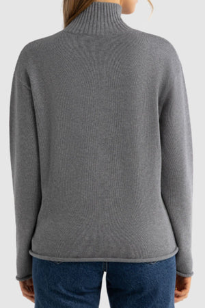 A person is seen from behind wearing a gray ORTC Astrid Knit Sweater with a high neck and blue jeans, set against a plain light background.
