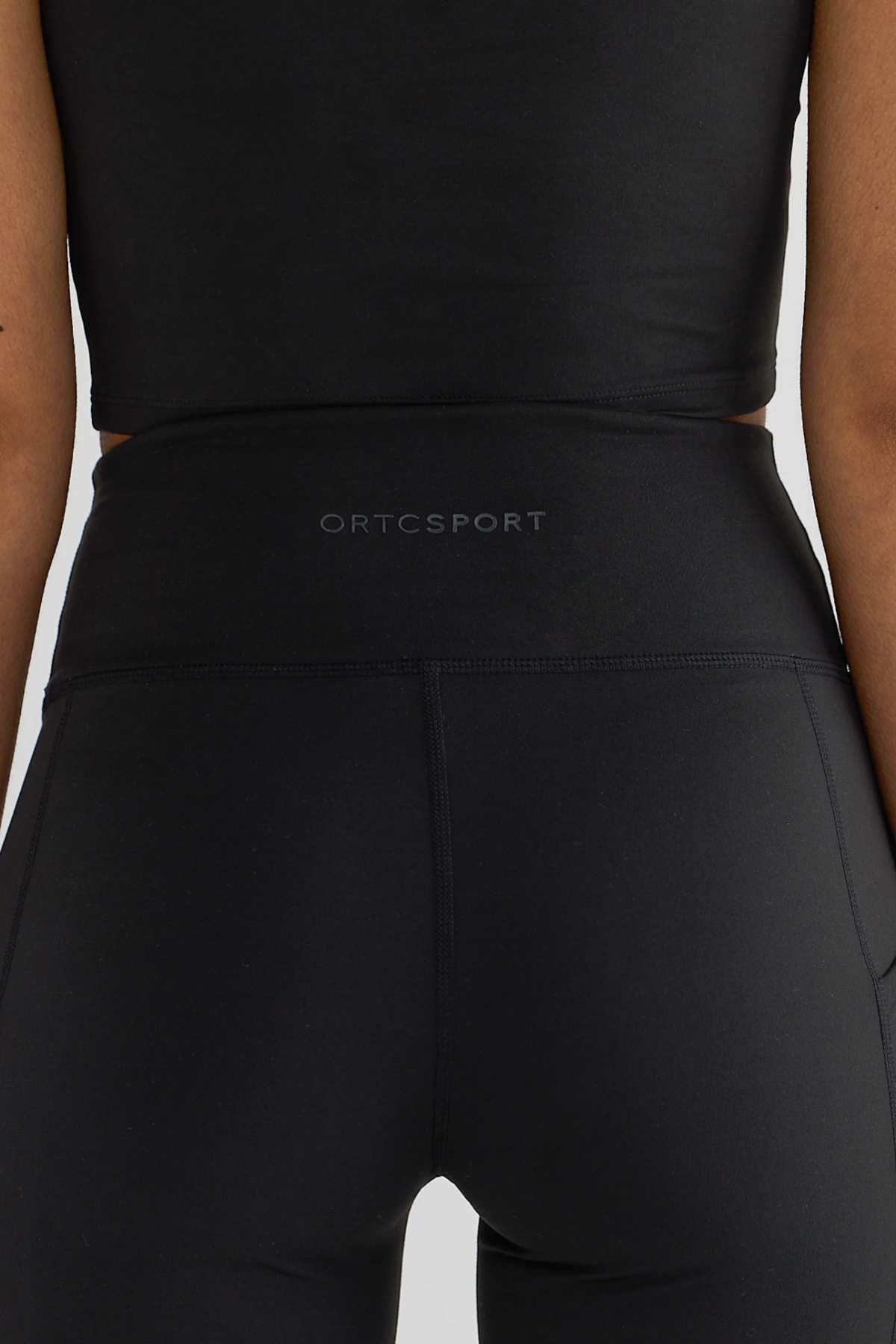 The image presents a close-up of a person wearing a black sports top paired with ORTC Eva 6 Inch Bike Shorts, featuring "ORTCSPORT" on the waistband. These high-waisted bike shorts are highlighted against the plain white backdrop, likely emphasizing the brand's chic athletic wear.