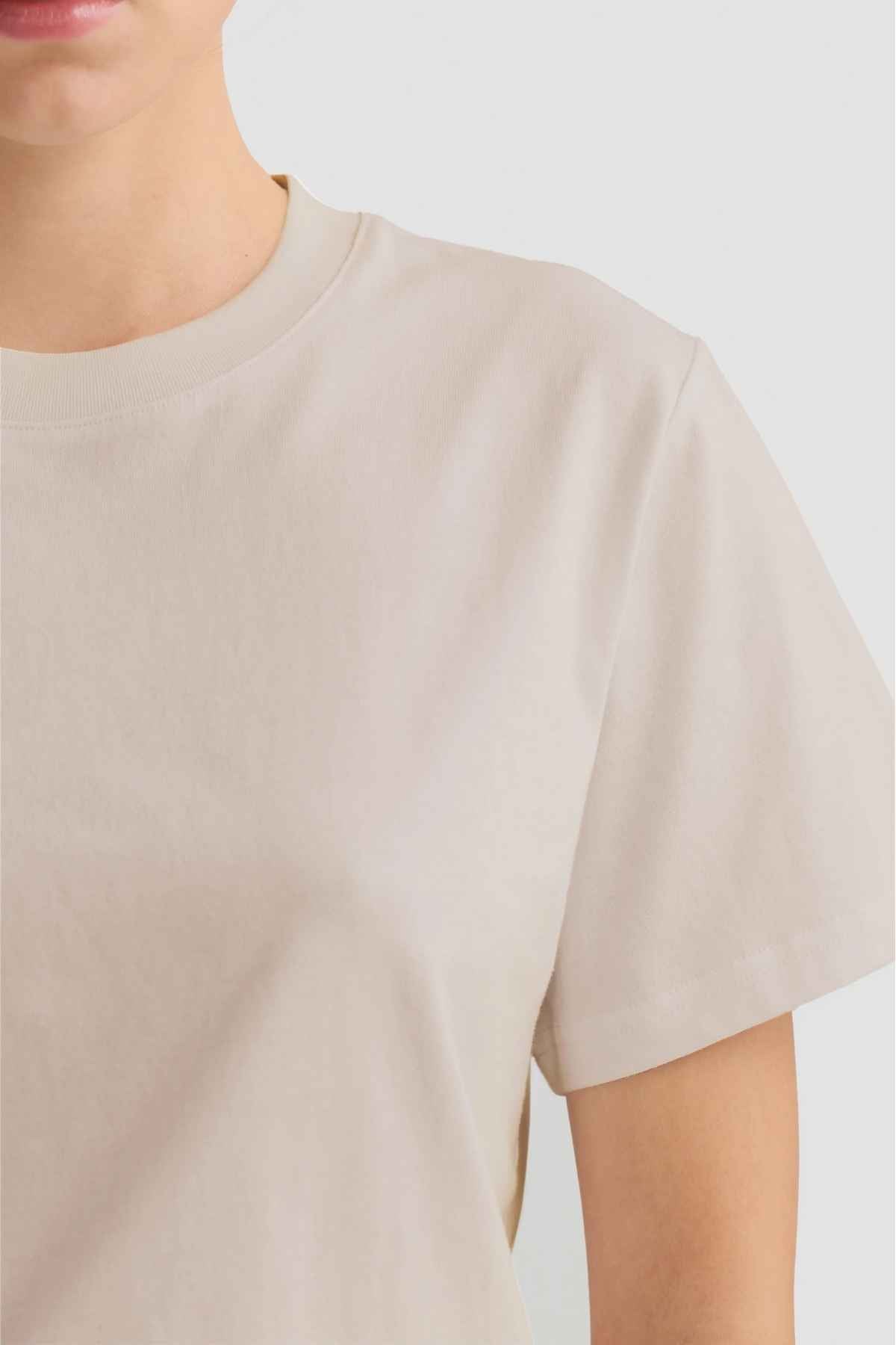 A person is wearing the ORTC Everyday T-Shirt in light beige, which has a relaxed fit and is crafted from mid-weight cotton. The image focuses on the upper body from shoulders to mid-chest, showcasing its short sleeves and round neckline.