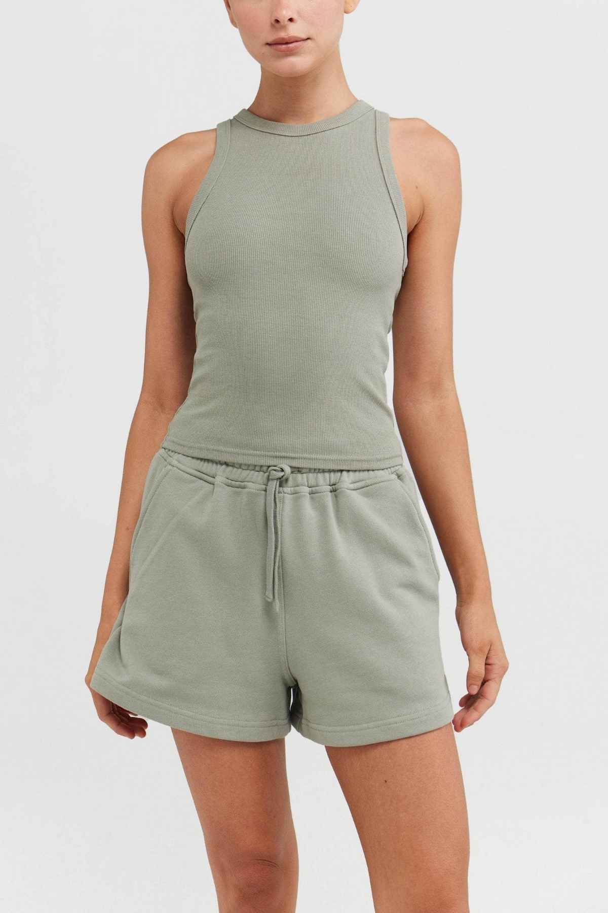The ORTC Mimi Rib Tank in light green, along with the matching shorts, presents a casual and comfortable style. Made from ribbed knit fabric, the sleeveless top and drawstring waist shorts are showcased against a simple, light-colored backdrop. The tank is ideal for layering.