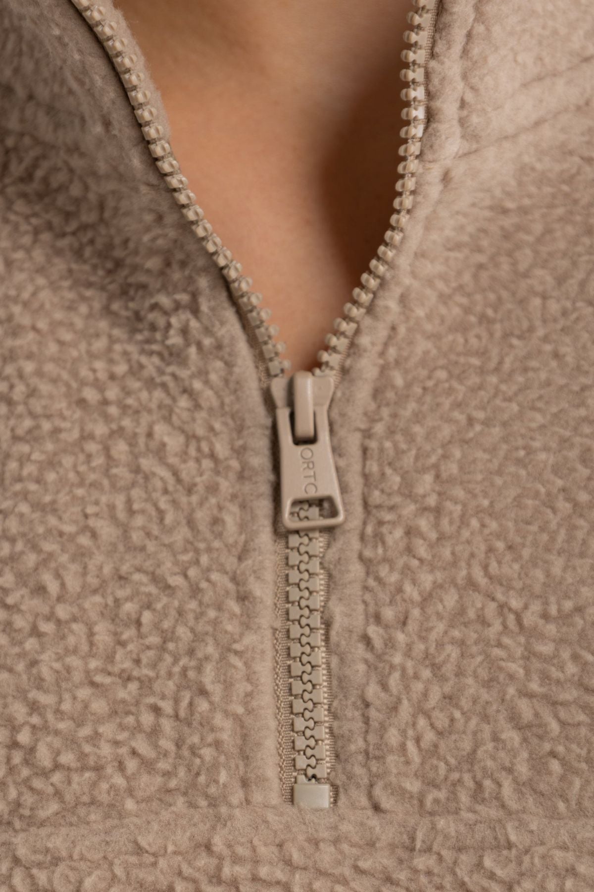 Close-up of the ORTC Sherpa Fleece Quarter Zip in light brown, featuring a partially unzipped zipper that reveals the textured sherpa fabric and a detail of the neck.