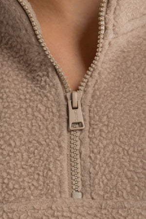 Close-up of the ORTC Sherpa Fleece Quarter Zip in light brown, featuring a partially unzipped zipper that reveals the textured sherpa fabric and a detail of the neck.