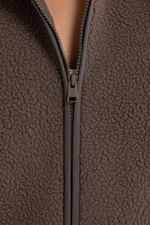 Close-up of the ORTC Sully Sherpa Fleece Vest in brown, featuring textured recycled polyester Sherpa and a partially unzipped front—ideal for cozy layering.