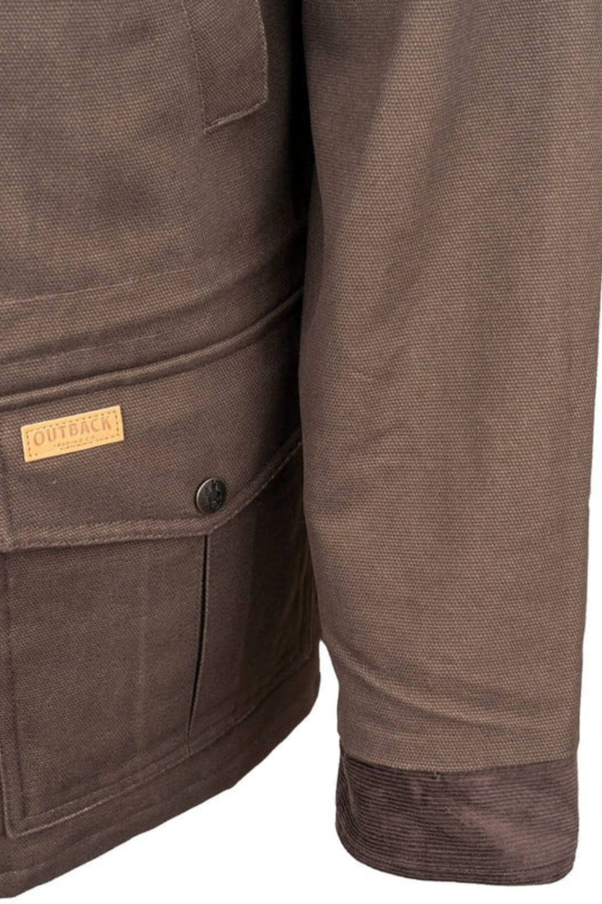 Close-up of the Outback Cattleman Jacket showcasing its detailed stitching. This brown outdoor companion includes multiple pockets, such as a flap pocket secured by a button and adorned with a small leather patch that reads "Outback." The cuff features reinforcement with darker fabric.