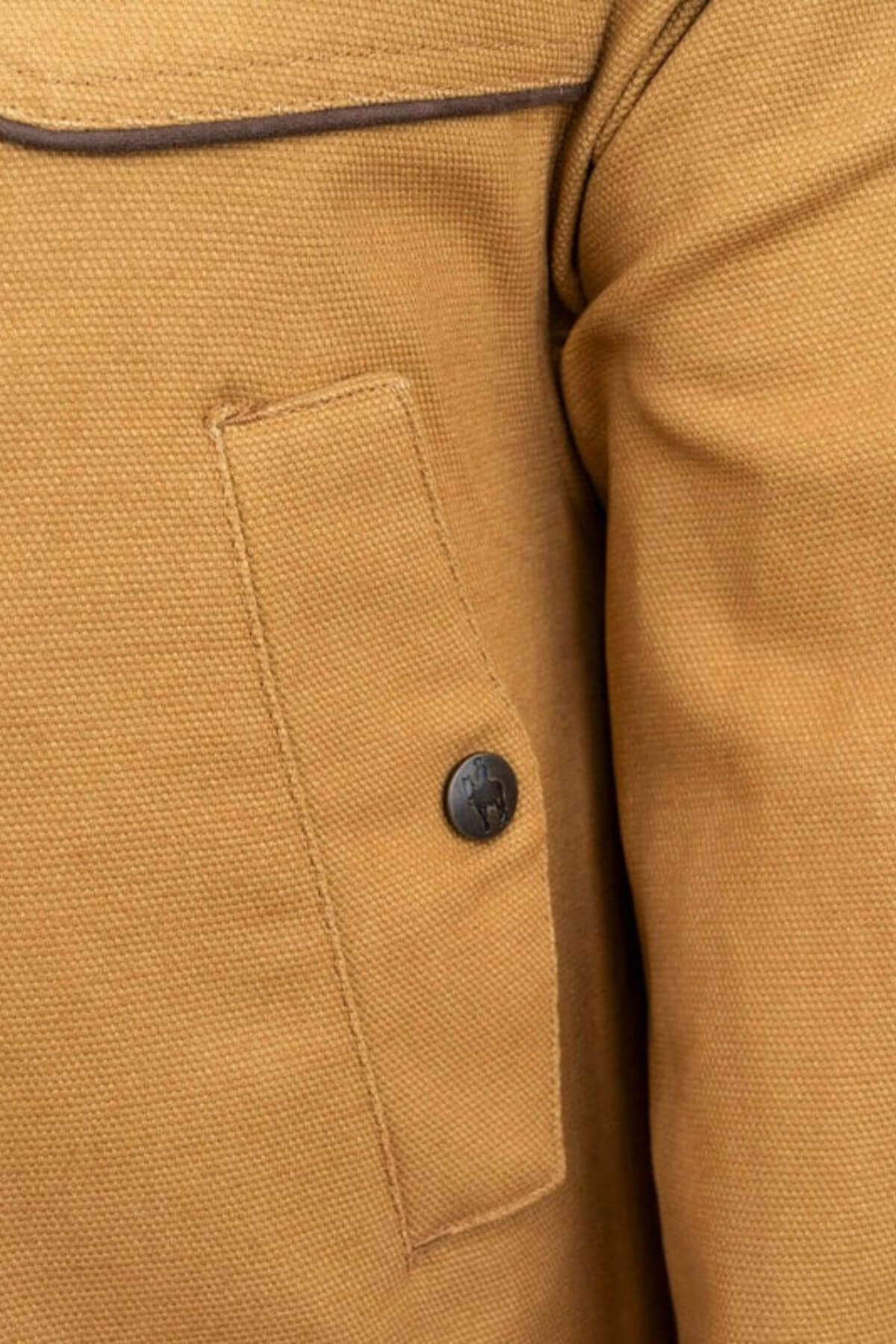 Close-up of an Outback Cattleman Jacket pocket featuring a flap secured by a black button. The fabric texture and seam details enhance its rugged charm, underscoring this multiple-pocket design as a reliable outdoor companion.
