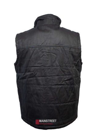 The Outback Heritage Oilskin Vest is black, sleeveless, and padded with a high Sherpa-lined collar. Displayed from the back, it features a red and white tag near the bottom reading "Mainstreet clothing destination." This weather-resistant vest offers warmth and style in any condition.